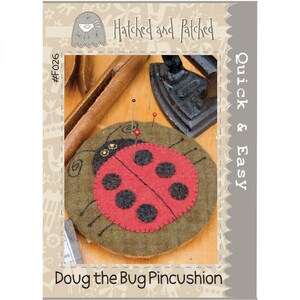 May include: A red and black ladybug pincushion with the text "Doug the Bug Pincushion" and "Quick & Easy" on a brown background. The pincushion is made of felt and has a green base.