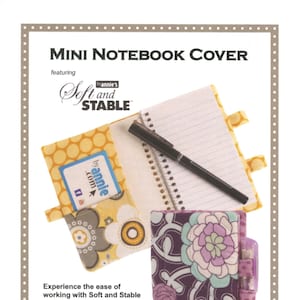May include: A sewing pattern for a mini notebook cover featuring Soft and Stable fabric. The cover is made with a floral fabric and has a pocket for business cards or credit cards. The pattern includes instructions for adding pen tabs to keep a pen handy.