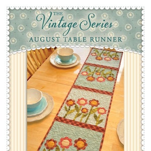 May include: A blue and brown table runner with a floral design. The table runner is made of fabric and has a quilted texture. The table runner is called "The Vintage Series August Table Runner" and is available from Shabby Fabrics.