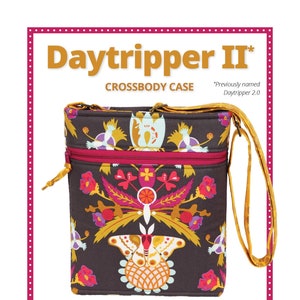 May include: A dark brown Daytripper II crossbody case with a colorful floral and bird pattern. The bag has a red zipper, a yellow strap, and the text "Daytripper II" at the top. The bag is designed for travel.