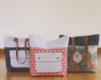 May include: Three tote bags with different fabric patterns. The bags are made of a light gray canvas with a zipper closure and a large pocket on the front. The bags have brown leather handles. The bags are sitting on a wooden floor. The text "CARAVAN TOTE + POUCH" is at the top of the image. The text "noodlehead" is at the bottom left of the image. The text "#534" is at the bottom right of the image.