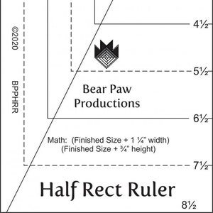 May include: A black and white ruler with markings for half inches and full inches. The ruler is labeled "Half Rect Ruler" and has the company name "Bear Paw Productions" printed on it. The ruler is made in the USA.