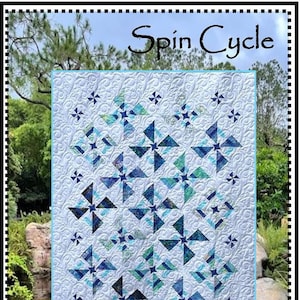 May include: A blue and white quilt with a "Spin Cycle" design. The quilt is made up of a repeating pattern of pinwheels. The quilt is surrounded by a green border and the text "Whirligig Designs" is at the bottom.