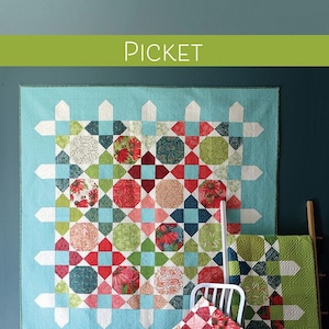 May include: A quilt pattern called "Picket" by Robin Pickens. The pattern is fat quarter or layer cake friendly. The quilt is made with a variety of colorful fabrics, including red, green, blue, and white. The quilt is displayed on a wall in a room with a wooden floor.