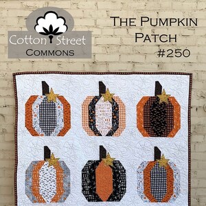 May include: A white quilt with nine orange, black, and white patchwork pumpkins. The quilt is titled "The Pumpkin Patch #250" and is a Cotton Street Commons design.