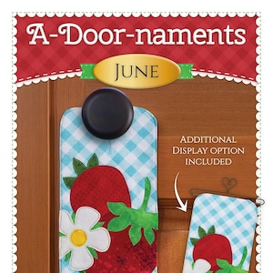 May include: A-Door-naments June door hanger featuring a strawberry design with a white flower and green leaves. The hanger is made of fabric and has a blue and white checkered background. The text "Additional Display Option Included" is also visible.