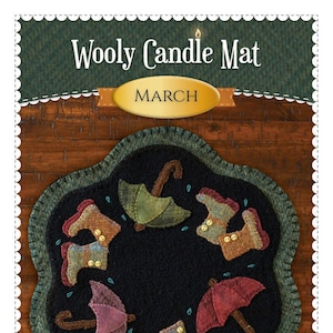 May include: Wooly Candle Mat with a black center, featuring appliqued umbrellas and boots in various colors. The mat is surrounded by a green border and includes the text "March". The Shabby Fabrics logo is visible.