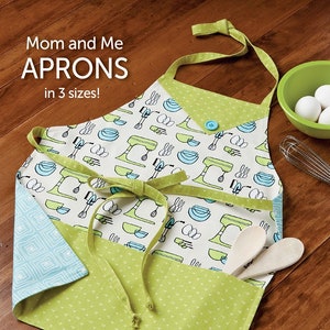 May include: A green and blue apron with a white background and a pattern of kitchen mixers and bowls. The apron has a pocket and ties. The text "Mom and Me Aprons in 3 sizes!" is at the top of the image. The text "BONUS! includes Chenille Hotpad!" is at the bottom of the image. The text "ATK-176" is in the bottom right corner of the image.