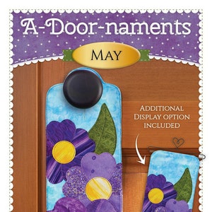May include: A-Door-nament door hanger with purple flower appliqués and a yellow center. The design includes a smaller matching display option. The text "MAY" is displayed on the door hanger. The brand name "Shabby Fabrics" is also visible.