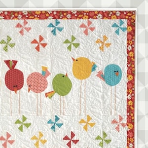 May include: A colorful quilt featuring six stylized birds in a row, each with a unique pattern and color. The birds are perched on thin stems against a white background with pinwheel accents. The quilt has a floral border and the word "Twitter".