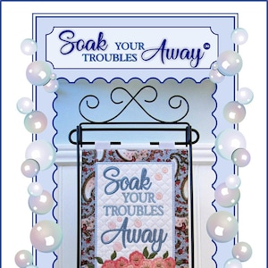 May include: A blue and white quilted wall hanging with the text "Soak Your Troubles Away" and a floral design. The hanging is on a black metal stand. A Janine Babich Design.