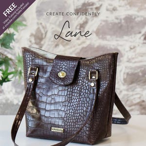 May include: A brown leather shoulder bag with a crocodile pattern. The bag has a flap closure with a magnetic snap or turn lock. The bag has a long shoulder strap and an inside slip pocket. The bag is called "Lane" and is a sewing pattern by Sallie Tomato.