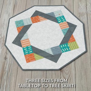 May include: A geometric quilt pattern with the text "GATHER ROUND" at the top. The quilt features a white center with a gray border and a design of colorful squares in orange, teal, and blue. The text "THREE SIZES FROM TABLETOP TO TREE SKIRT!" is also visible.