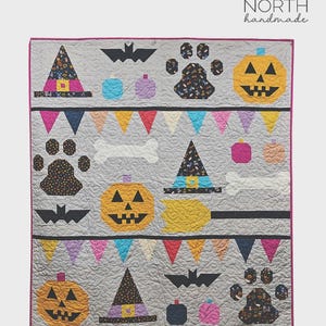 May include: A gray quilt titled Halloween Paw-ty measuring 64 inches by 72 inches. The quilt features appliqued patterns of orange jack-o'-lanterns, black bats, white bones, colorful paw prints, witch hats, and pennant banners on a gray background.