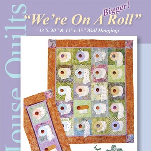 May include: A quilt with the text "We're On A Roll" and dimensions of 33" x 40" and 15" x 35". The quilt features a repeating pattern of toilet paper rolls on a patchwork background. The quilt is bordered with a brown fabric. The image also includes a smaller quilt with a similar design.