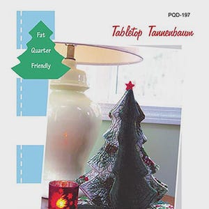 May include: A tabletop Christmas tree made of fabric, with a red star on top. The tree is approximately 13 inches tall and has a 12-inch diameter tree skirt. The image also includes a lit candle and the text "Tabletop Tannenbaum".