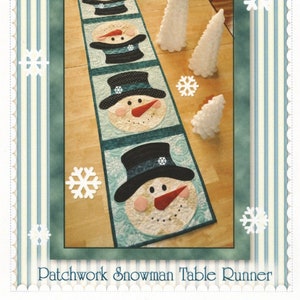 May include: Patchwork snowman table runner with four snowmen in black hats and red noses. The table runner is on a wooden table with white decorative trees.