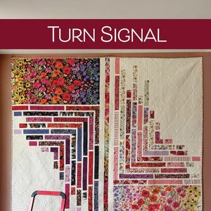 May include: A large quilt with the text "TURN SIGNAL" at the top. The quilt features floral and geometric patterns in red, purple, and white. A red ladder is in front of the quilt. The text "2 1/2" x WOF Jelly Roll-friendly" is also visible.