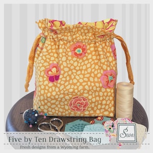 May include: A fabric drawstring bag featuring a yellow and white spotted pattern with pink and orange floral accents. The bag includes a ruffled top edge and matching yellow drawstrings. Text on the image reads Five by Ten Drawstring Bag.