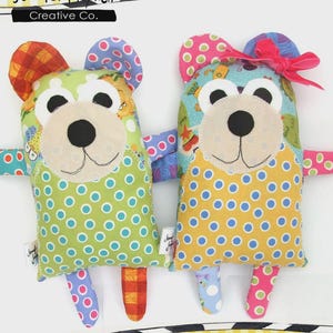 May include: Two handmade bear-shaped plush toys. One bear has a green body with blue polka dots, the other has a yellow body with blue polka dots. Both have colorful patterned ears, arms, and legs. The text "Quincy and Maggie" is at the bottom.