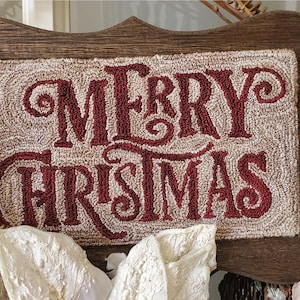 May include: A wooden sign with a cream-colored background and the words "Merry Christmas" in red yarn lettering. The sign is framed with a dark brown wood frame.