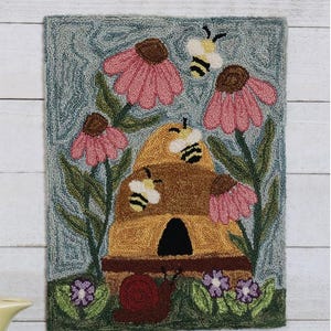 May include: A needlepoint rug depicting a beehive with bees and flowers. The beehive is yellow and brown with a black entrance. The flowers are pink and white with green stems and leaves. The background is blue.