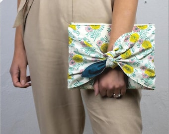 May include: A white clutch bag with a floral print in shades of yellow, pink, and green. The bag is tied with a teal ribbon and has the text "briar bag" printed below it.