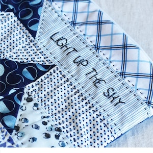May include: A blue and white patchwork fabric pouch with a zipper closure. The pouch has a stitched label that says "Light up the sky".