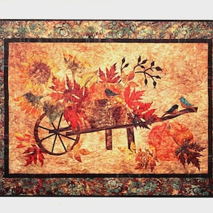 May include: A fall-themed wall hanging featuring a wheelbarrow filled with autumn leaves and pumpkins. Two small birds perch on a branch. The quilt is approximately 38 inches by 28 inches, with the text "Harvest Pumpkin".