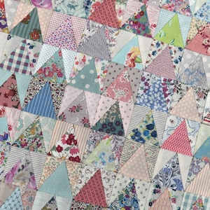 May include: A patchwork quilt made of various floral and geometric patterned fabrics in shades of pink, blue, green, and white. The quilt is made of triangular pieces sewn together to create a repeating pattern.