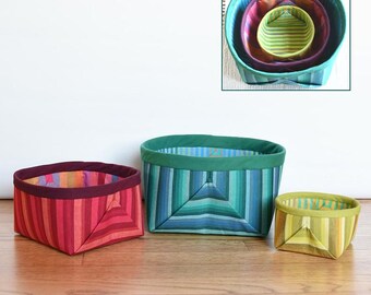May include: Three fabric storage baskets in different sizes, 4 inches, 6 inches, and 8 inches square, with colorful striped patterns. The baskets are nested inside each other. The image includes the text "Nestlings" and "ATB-183".