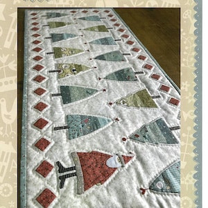 May include: A quilted table runner featuring a row of Christmas trees in shades of green and blue, with a Santa Claus figure at the bottom. The table runner has a red and white diamond border. The text "O Christmas Tree Table Runner" is at the bottom of the image.