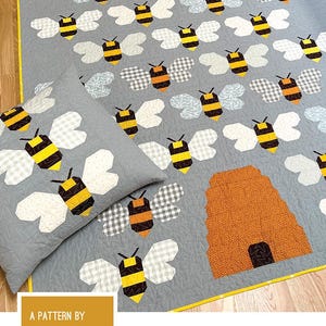 Puede incluir: Un patrón de acolchado para una colcha y una almohada en forma de colmena. El patrón presenta un fondo gris con abejas de patchwork amarillo y negro y una colmena marrón y naranja.