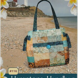 May include: A patchwork handbag with a blue button closure and matching handles. The bag features a variety of patterned fabrics in shades of blue, brown, and beige. The text "Hamptons Handbag" is displayed below the bag, with the words "Pink Sand Beach Designs" at the top.