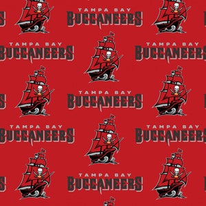 May include: A red background with a repeating pattern of the Tampa Bay Buccaneers logo. The logo features a pirate ship with a skull and crossbones, and the words "Tampa Bay Buccaneers" in black text.