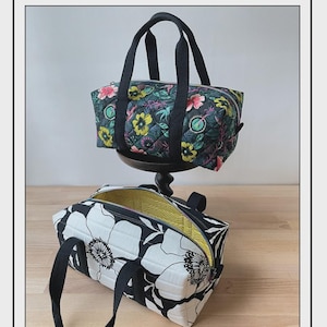 May include: Two mini duffle bags with black handles. One bag features a floral pattern with pink, yellow, and green flowers on a dark background. The other bag has a black and white floral design. The text "Bodobo Bags" and "Simple Mini Duffle" are also visible.