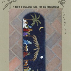 May include: A blue and green fabric wall hanging with a nativity scene. The scene includes a star, a crescent moon, palm trees, and figures of people and animals. The text "# 357 FOLLOW ME TO BETHLEHEM" is printed at the top of the image.