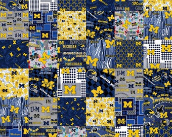 May include: A patchwork fabric featuring a variety of designs and colors, including blue, yellow, and white. The fabric features the University of Michigan logo and the words "Go Blue", "Michigan Wolverines", and "Let's Go Blue".