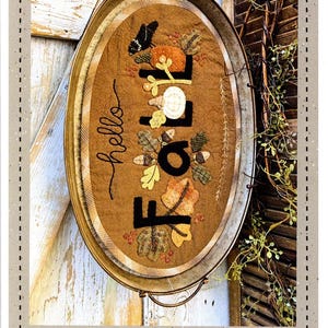 May include: A brown felt table mat or tray liner with the words "hello fall" embroidered in black thread. The mat is decorated with felt leaves, acorns, and a bird. The mat is 12.5 inches by 20 inches.