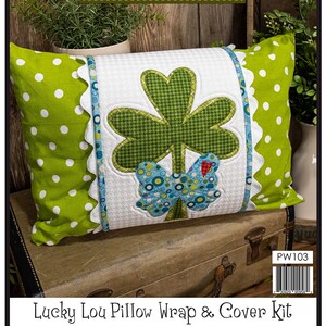 May include: A green and white pillow with a shamrock and butterfly applique. The pillow is part of a Lucky Lou Pillow Wrap & Cover Kit. The kit includes instructions, precut fused applique, notions, fabric, and a tea towel for the pillow and wrap. The finished size of the applique is 7 1/2 inches by 10 1/8 inches, the pillow is 13 inches by 18 1/2 inches, and the pillow wrap is 9 inches by 30 inches.  @Leanne Anderson 2022