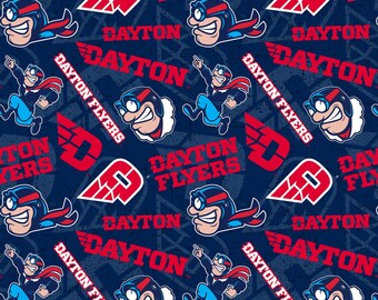May include: A blue and red patterned fabric with the words "Dayton Flyers" repeated throughout. The pattern also includes a cartoon character wearing a red scarf and goggles.