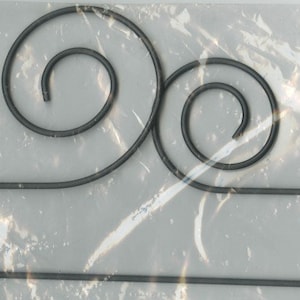 May include: A black metal hanger with two decorative swirls at the top. The hanger is designed to hold a variety of items, such as scarves, hats, or jewelry.