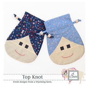 May include: Two fabric drawstring bags with a smiling face design. The bags are made of blue and white floral fabric. The text "Top Knot" and "Fresh designs from a Wyoming farm." is printed below the bags.
