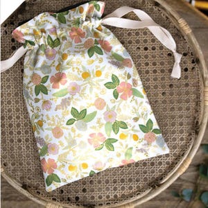 May include: A white drawstring bag with a floral print in shades of pink, yellow, and green. The bag is sitting on a woven basket. The text "it's a cinch learn to sew: beginner drawstring bag" is printed below the image.