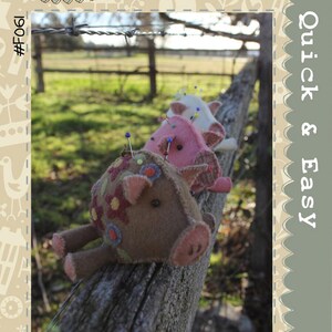 May include: Three handmade pin cushion pigs rest on a weathered wooden fence. The front pig is brown with floral accents, while the others are pink and white. The image includes text that reads "Hatched and Patched" and "Quick & Easy."