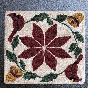 May include: A cream-colored needlepoint canvas with a red poinsettia, green holly leaves, and two red cardinals. The design is surrounded by a border of gold bells. The text "Garden Gals December" is at the bottom of the canvas.
