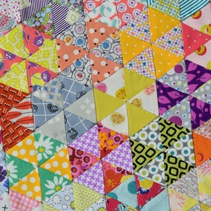 May include: A colorful quilt made of many different fabric scraps, featuring a geometric pattern of triangles. The quilt is made in a variety of colors, including pink, yellow, green, blue, and purple.