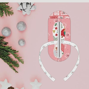 May include: A craft pattern for a Ballerina Slipper Pouch by Sew A Story. The design features a pink pouch with a central zipper, decorated with illustrations of ballerinas and holiday motifs. The finished size is 3.25 inches by 7.5 inches by 3 inches.