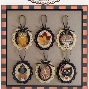 May include: Six felt ornaments with black ribbon hangers, each featuring a different fall-themed design: an owl, a leaf, a pumpkin, a bird, a pumpkin face, and a black cat. The ornaments are arranged in two rows of three. The title "Festive Fall Ornaments #280" is written below the ornaments.
