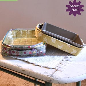 May include: Two fabric-covered baskets for 9x9 and 9x13 inch baking pans. The baskets are made with a floral print and a yellow print with chickens. The text "Pass the Hot Dish!" is at the top of the image. The text "Stores Flat!" is in a purple starburst shape.